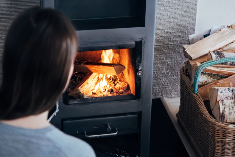 Over the shoulder look of woman tending a wood fired fireplace