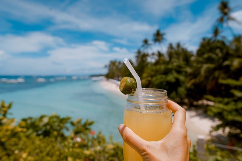 Person holding tropical cocktail by the beach