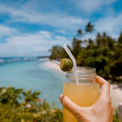 Person holding tropical cocktail by the beach