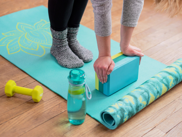 Person stretching on yoga mat with yoga block beside hand weight and water bottle