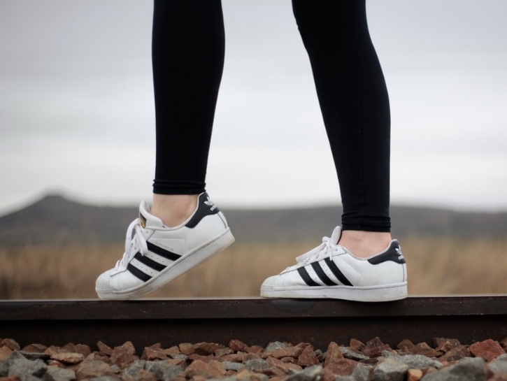 Person walking on railroad track with black leggings and white and black adidas