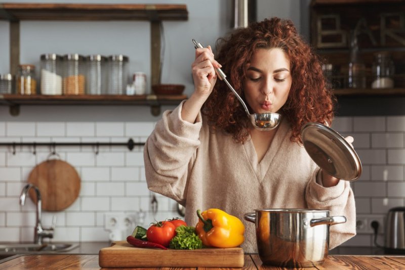 Photo of pretty caucasian woman holding cooking ladle spoon while eating soup with fresh vegetables in kitchen at home