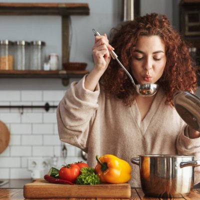 Photo of pretty caucasian woman holding cooking ladle spoon while eating soup with fresh vegetables in kitchen at home