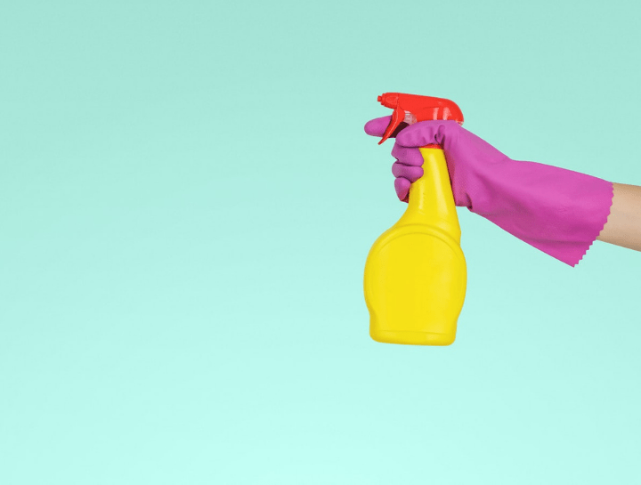 pink gloved hand holding yellow spray bottle