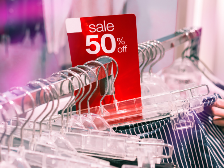 Red sales tag on clothing rack with hand holding striped clothing on hanger