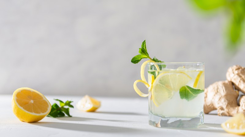 Refreshing lemonade with lemon, mint, ginger and ice in glass and bottle on white concrete background. Summer refreshing drink. Cold detox water with lemon