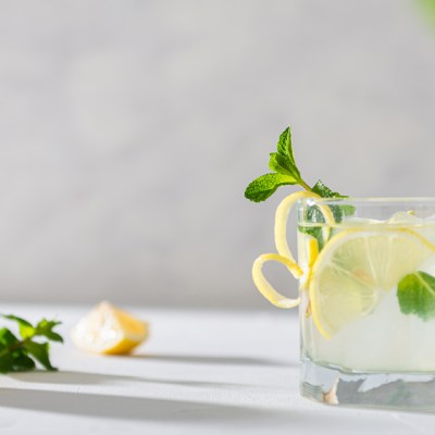 Refreshing lemonade with lemon, mint, ginger and ice in glass and bottle on white concrete background. Summer refreshing drink. Cold detox water with lemon