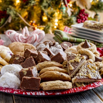 Rustic holiday party table with tray of homemade cookies and candy with holiday napkins and plates in front of Christmas tree