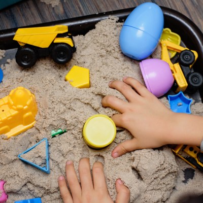 Sensory bin for sensory play. Child playing with kinetic sand and toy construction machinery. Hand of child in sand close up. Activity for fine motor development