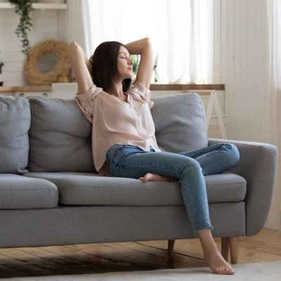 Serene lady housewife lounge sit on sofa feel fatigue napping hold hands behind head, calm young woman rest on comfort couch with eyes closed breath fresh air in cozy clean modern living room at home