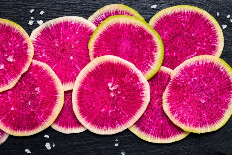 sliced watermelon radish with sea salt on black background. . top view