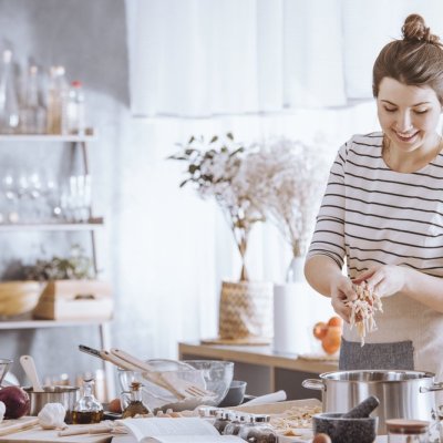 Smiling young woman adding noodles to pot while cooking in the kitchen