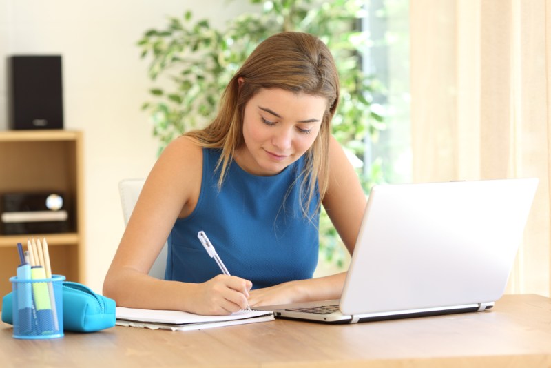 Student studying writing notes in a notebook in a table at home