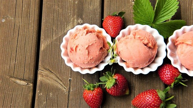 three containers of strawberry ice cream and loose strawberries
