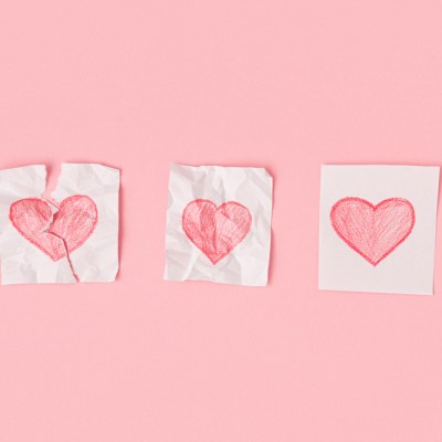 Three hearts drawn on pieces of paper on a pink background. One heart is torn, the second is crumpled, the third is whole. Progress of love.