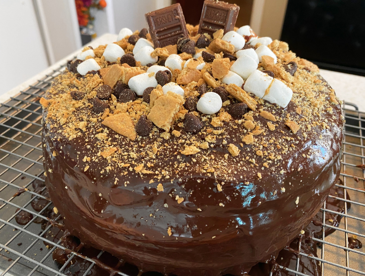 three layer s'mores cake covered in chocolate ganache graham crackers chocolate chips and Hershey's bars