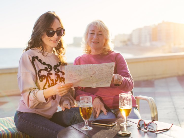 Tourists (mom and daughter) viewing a map while drinking beer at beach cafe - family and travel concept