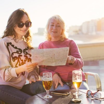 Tourists (mom and daughter) viewing a map while drinking beer at beach cafe - family and travel concept