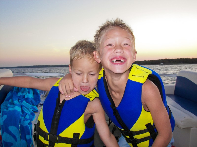 Two boys on a boat wearing life vests at sunset