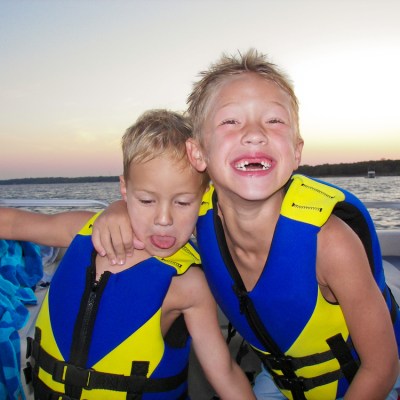 Two boys on a boat wearing life vests at sunset