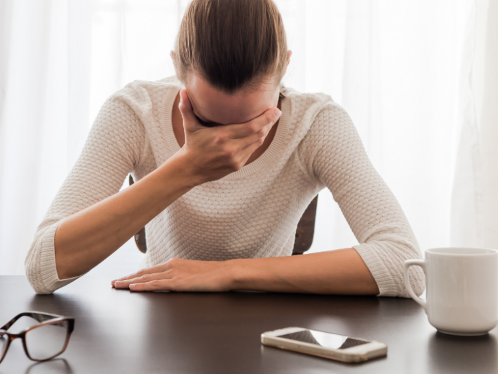 Woman at desk holding her head in her hand