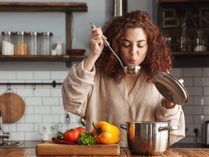 Woman cooking and holding up a spoon to blow on her food