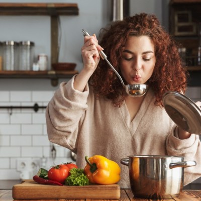 Woman cooking and holding up a spoon to blow on her food
