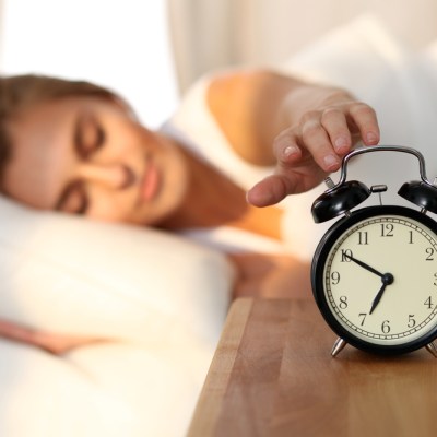 woman hitting snooze on alarm clock