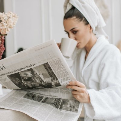 woman in white robe reading newspaper and drinking coffee