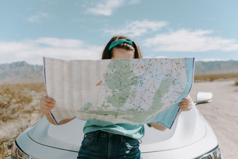 woman leaning on car looking at map