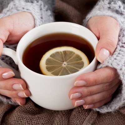 Woman's hand holding cup of tea with lemon on a cold day