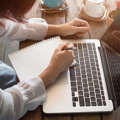 Woman studying with laptop and taking notes on a desktop at cafe