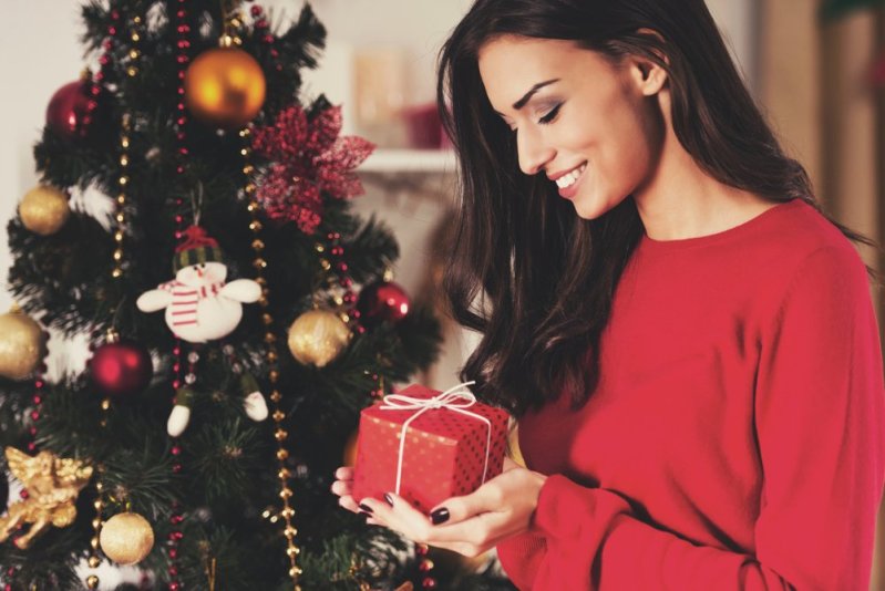 Woman Watch at Christmas Present. Portrait of Young female. Preparations for Celebration. Happiness at Home. Profile View. Holiday Concept. Caucasian Young Woman. Decorating Christmas Tree.