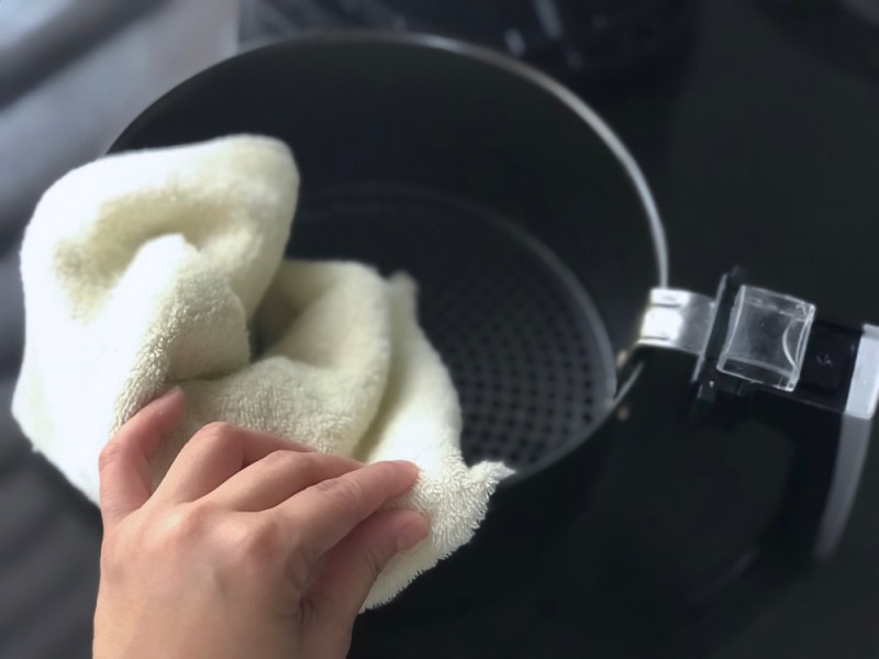 Women’s hand wipe the air fryer basket with kitchen towel.Selective focus at the hand and towel with depth of field camera effect.Black background. This image may contain noise due low light condition