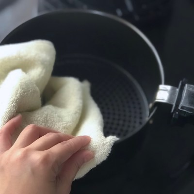 Women’s hand wipe the air fryer basket with kitchen towel.Selective focus at the hand and towel with depth of field camera effect.Black background. This image may contain noise due low light condition