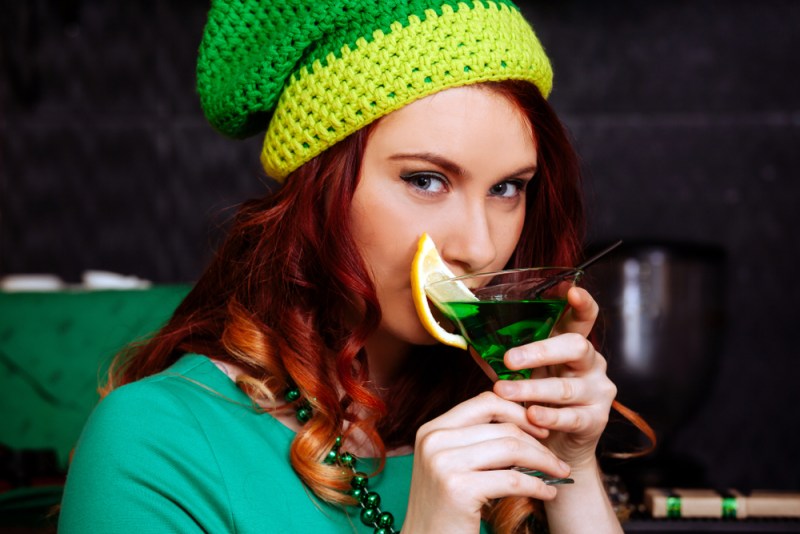Young girl celebrate St. Patrick's Day. Woman have fun at the bar. A beautiful girl in a green hat and dress drinks a green cocktail.