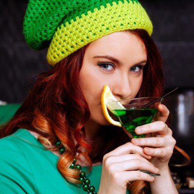 Young girl celebrate St. Patrick's Day. Woman have fun at the bar. A beautiful girl in a green hat and dress drinks a green cocktail.