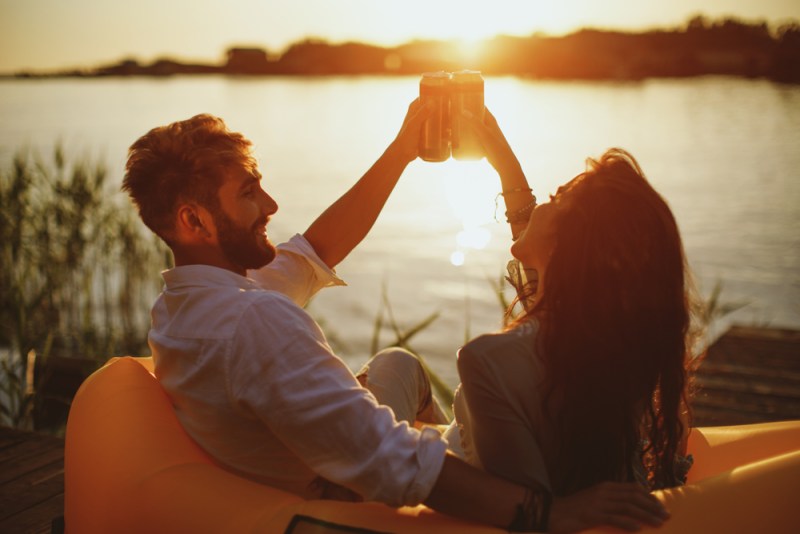 Young happy couple enjoy canned wine by the river during the sunset