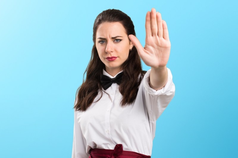 Young beautiful waitress making stop sign on colorful background