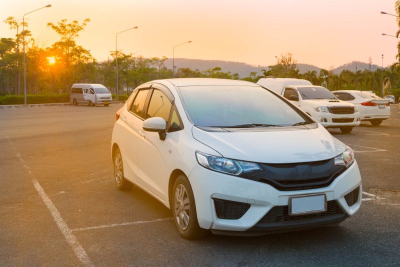 Cars parked in outdoor parking lot at a park in the evening time with sunlight of sunset and beautiful orange sky background