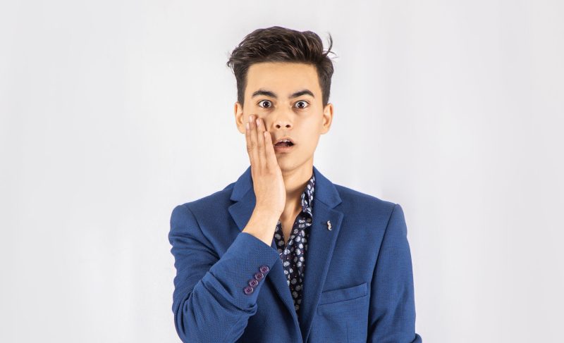 Photo of shocked man in blue blazer standing in front of white background