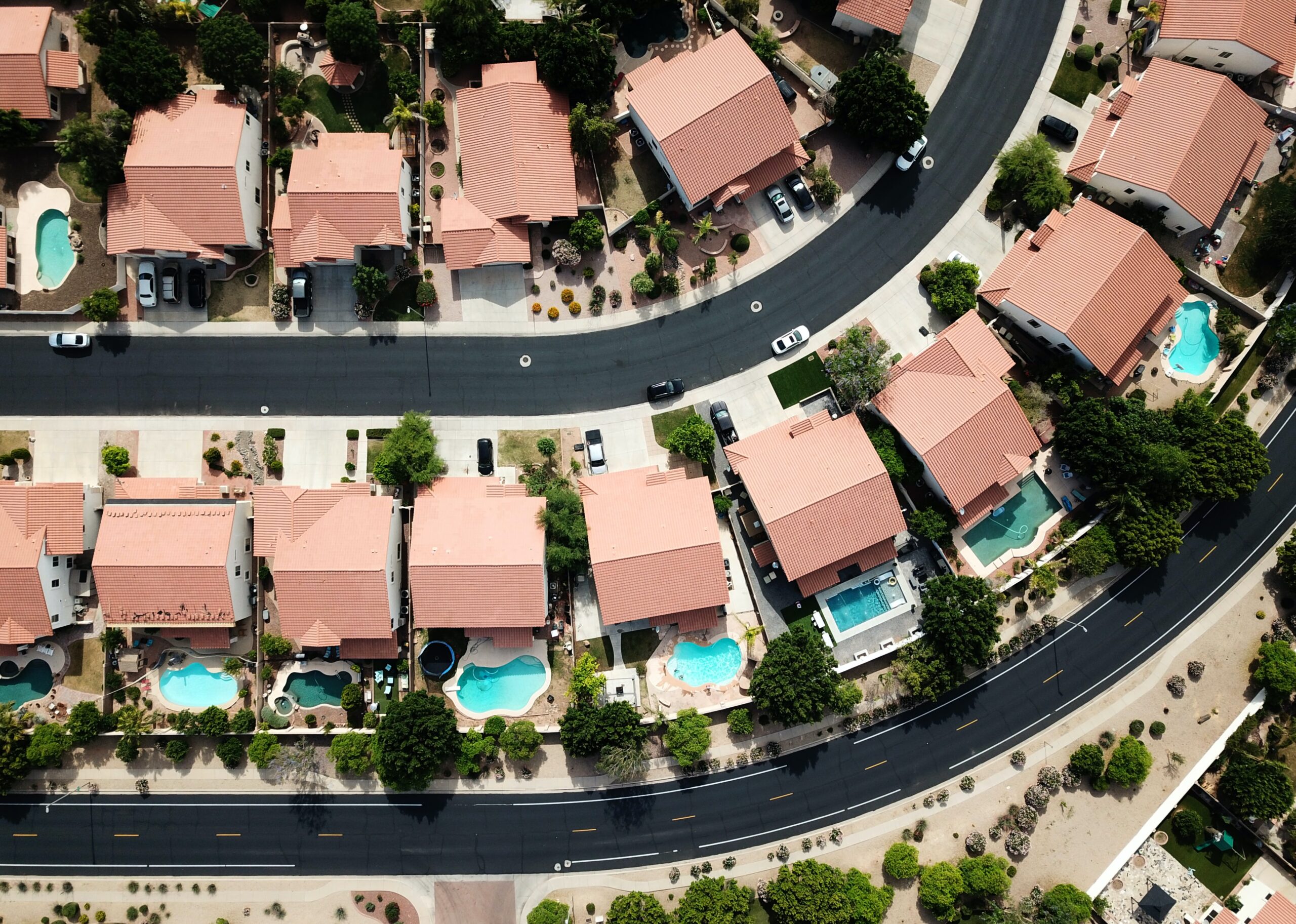 Flying high over a subdivision with tons of pools in backyards. Just take a look at the middle line of homes, they all have pools!