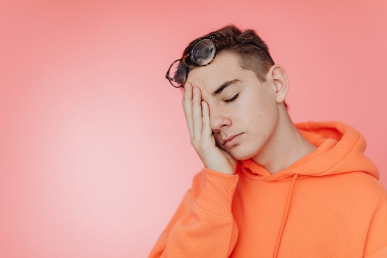 Man in orange hoodie holding hand on face