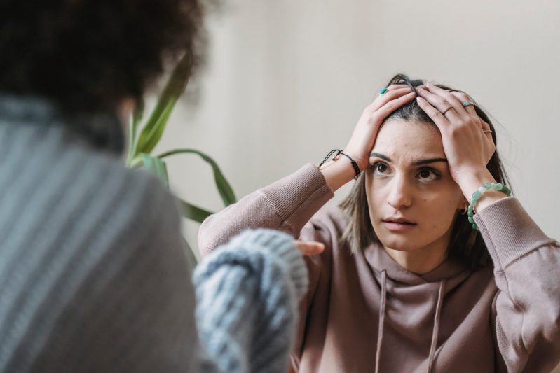 Anxious woman touching head while looking at crop female during argument