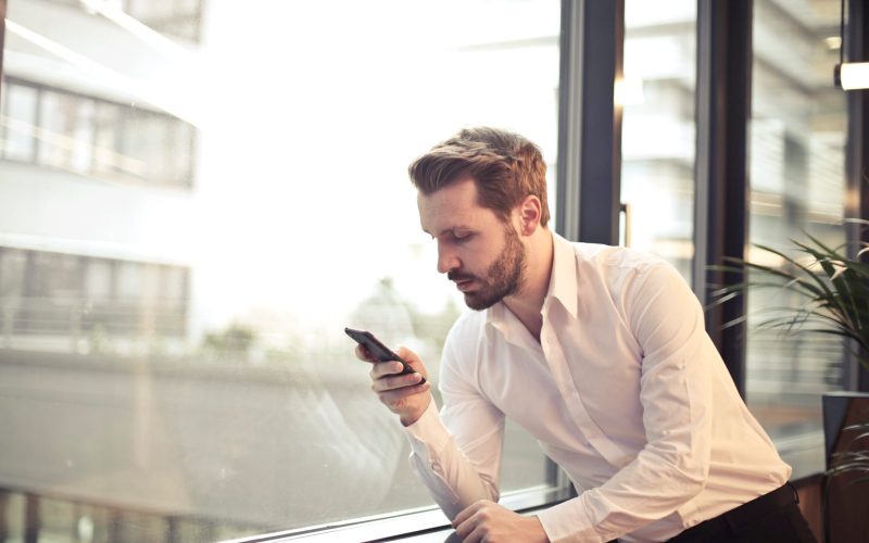 Photo of man in white dress shirt holding phone near window