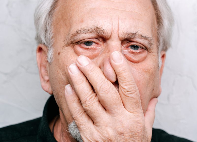Elderly man in black shirt covering his face
