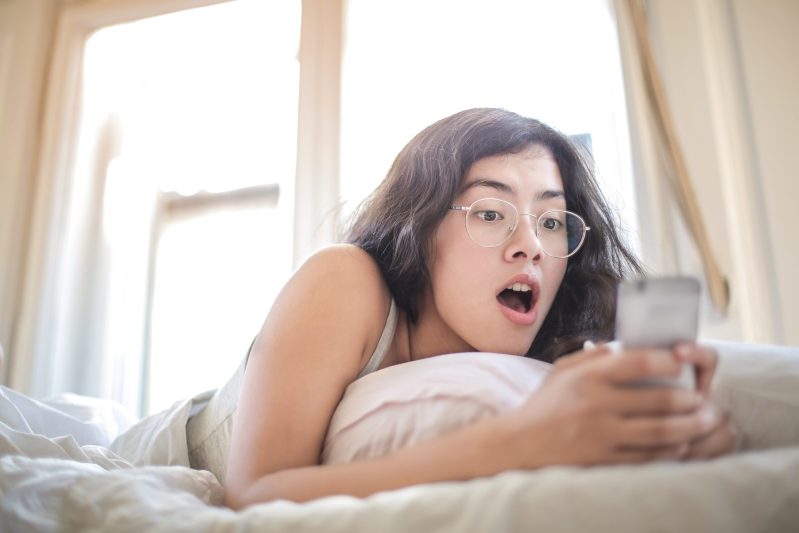 Woman lying on bed holding smartphone