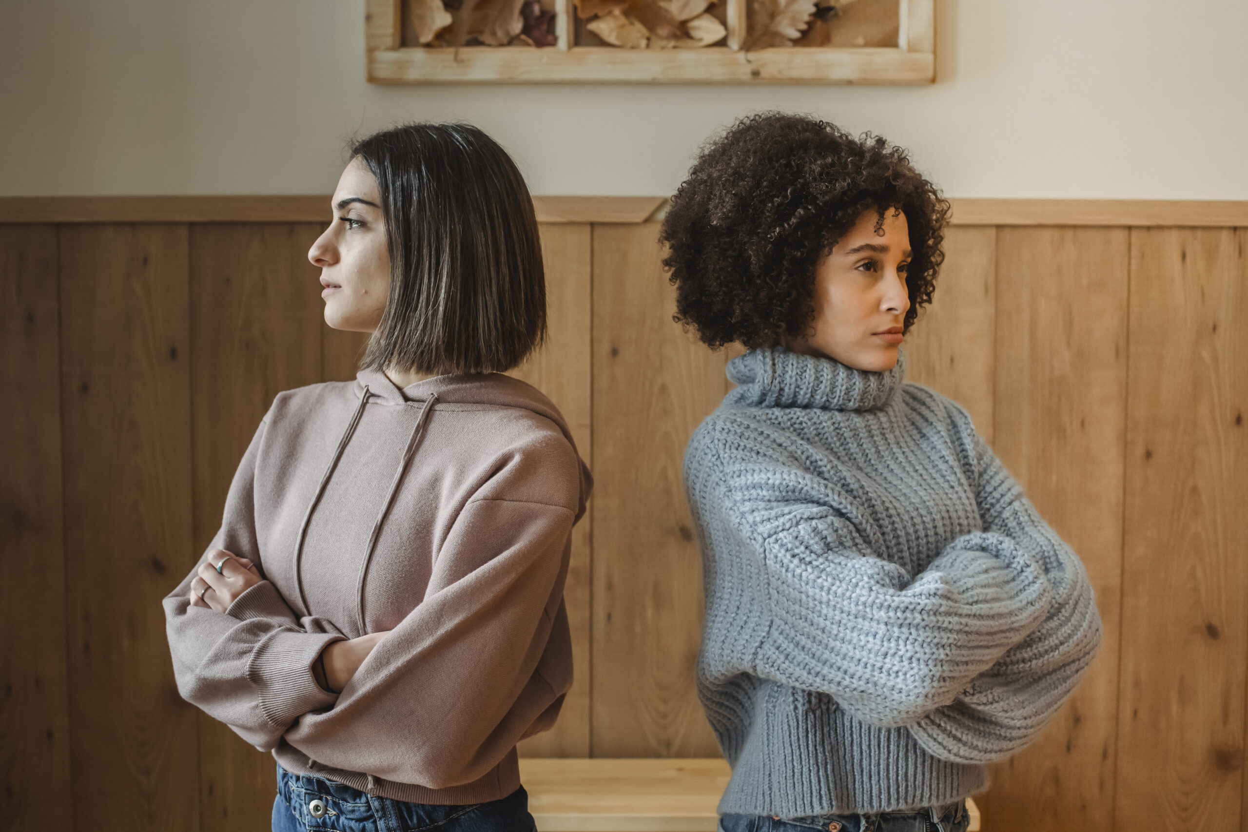Unhappy multiethnic women standing back to back in room