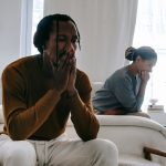 Unhappy black couple sitting on bed after having argument