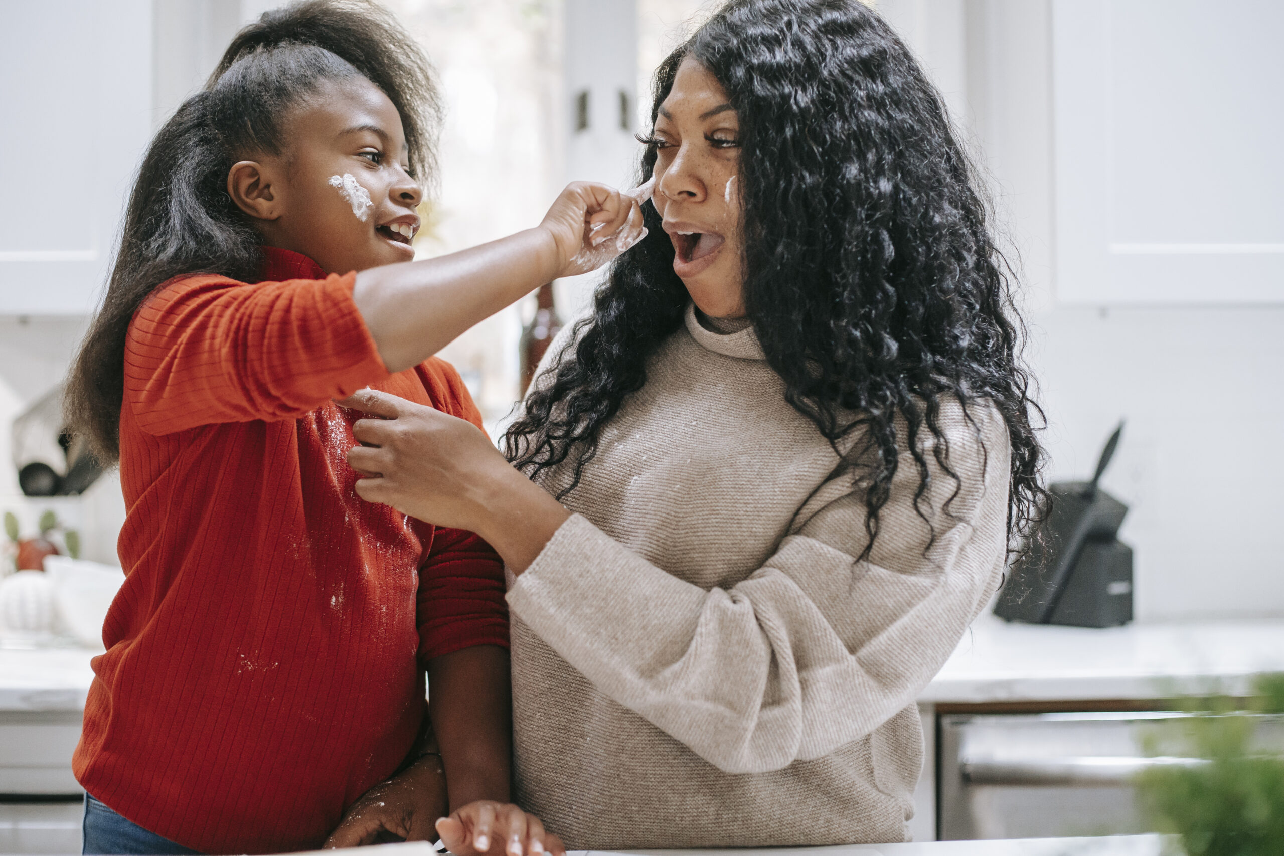 Carefree black girl applying flour on face of crop mother